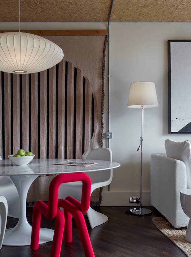A contemporary white living room showcasing a vibrant red chair alongside a minimalist white table, exuding elegance.