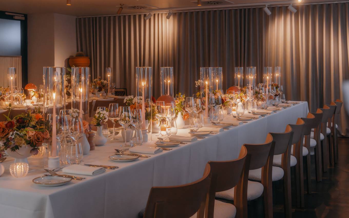 A long table elegantly set with white linens and flickering candles, creating a warm and inviting atmosphere.