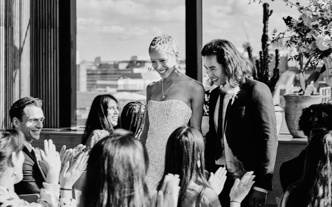 A bride and groom joyfully celebrate their wedding surrounded by smiling guests in a festive atmosphere.