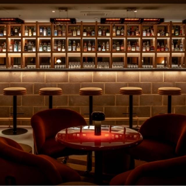 A sophisticated bar featuring red chairs and shelves stocked with various liquor bottles.