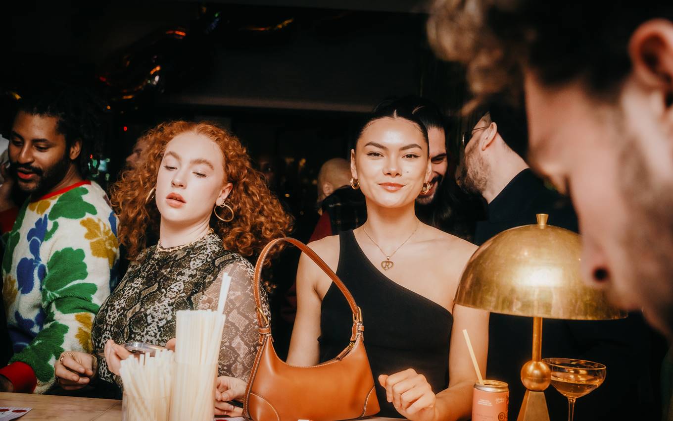 Guests socializing at a London bar with drinks, a warm lamp, and festive expressions enhancing the lively mood.