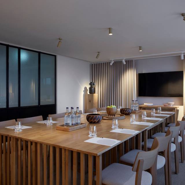 Sleek meeting room in central London with wooden table, bottled water, glasses, and a large screen with minimalist decor.