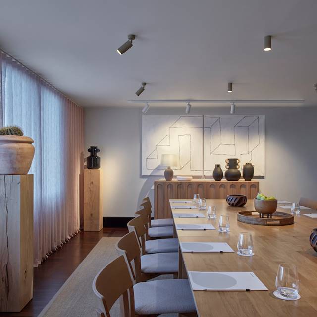 A long table surrounded by chairs, with a painting elegantly displayed on the wall behind it.
