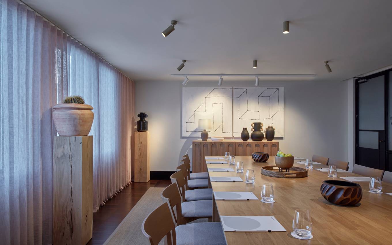 A long table surrounded by chairs, with a painting elegantly displayed on the wall behind it.