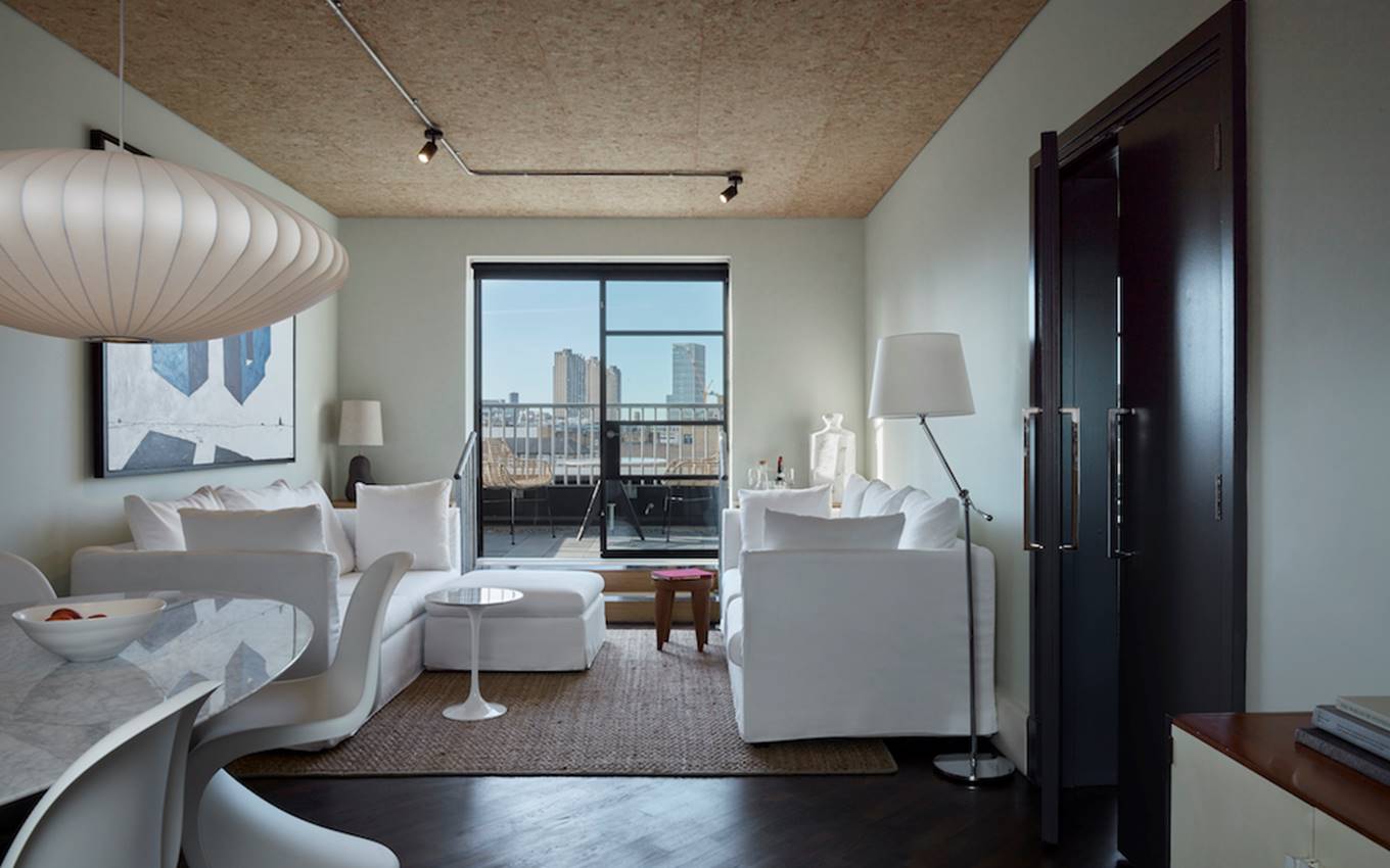 A modern living room featuring white furniture and a panoramic view of the city skyline through large windows.