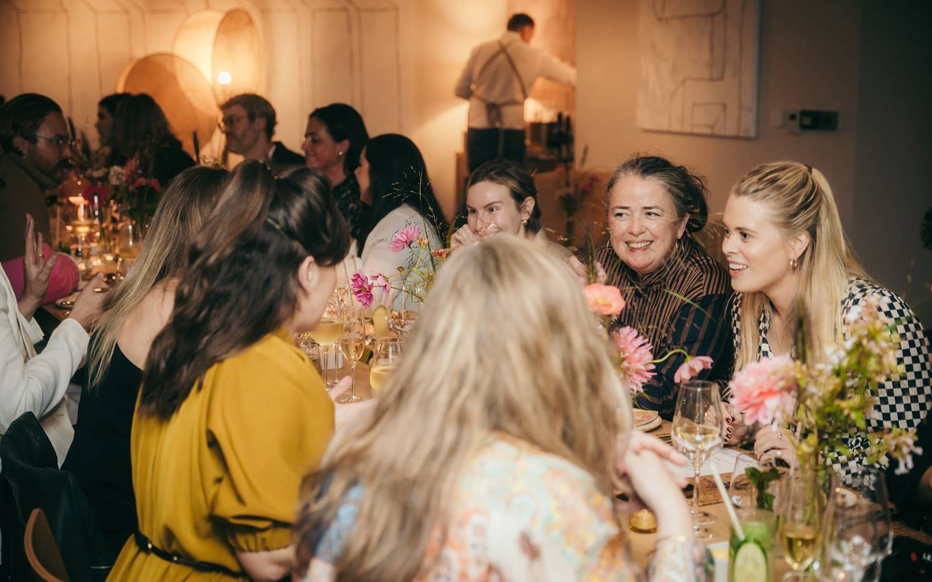 A group of women gathered around a table adorned with flowers, engaged in conversation and enjoying each other's company.