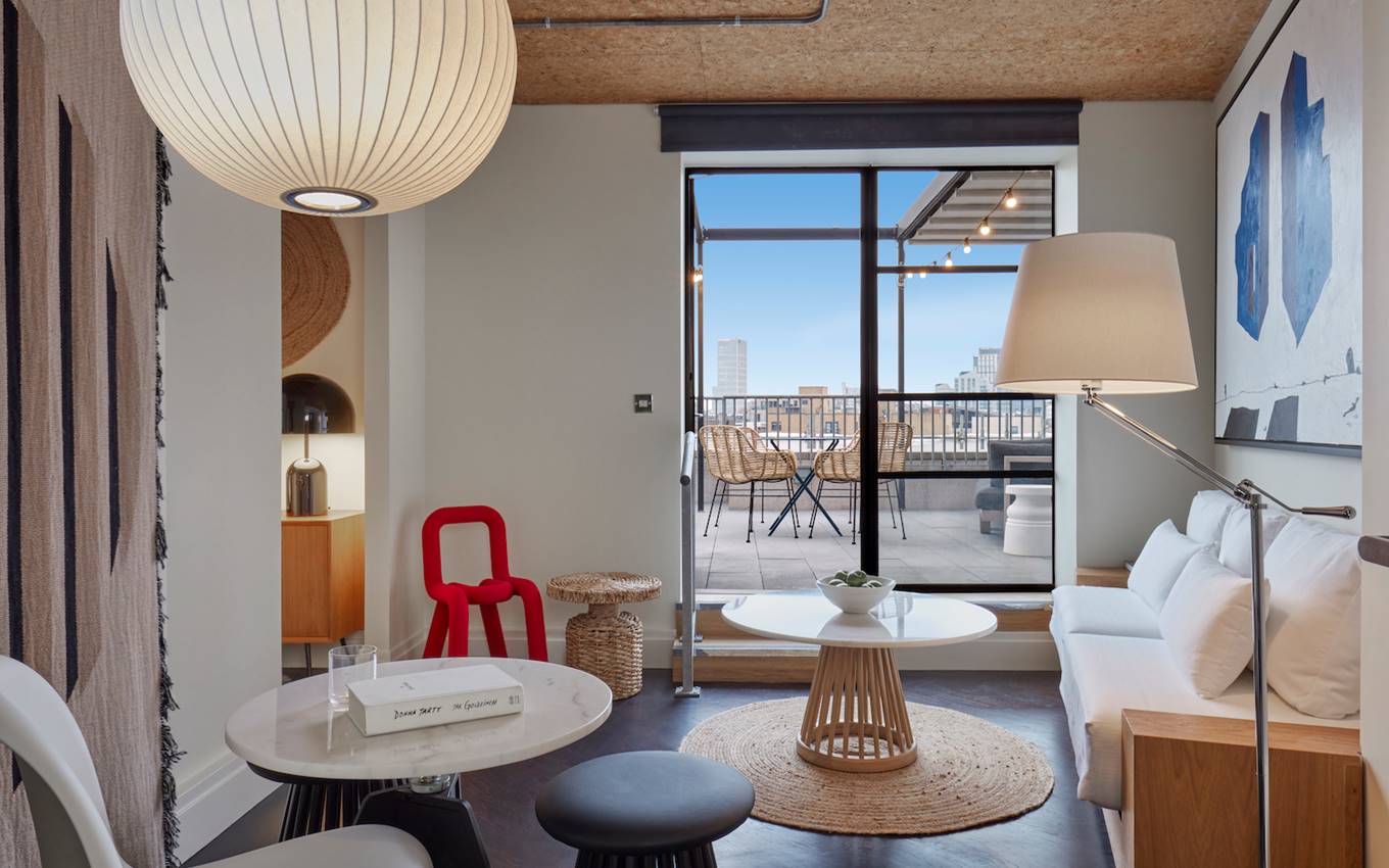 A contemporary hotel suite in London with a mix of modern and rattan furniture, leading to a private balcony with city views.